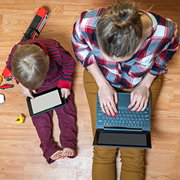 Woman on laptop and toddler on tablet