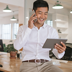 Man talking on a cell phone while looking at a tablet.