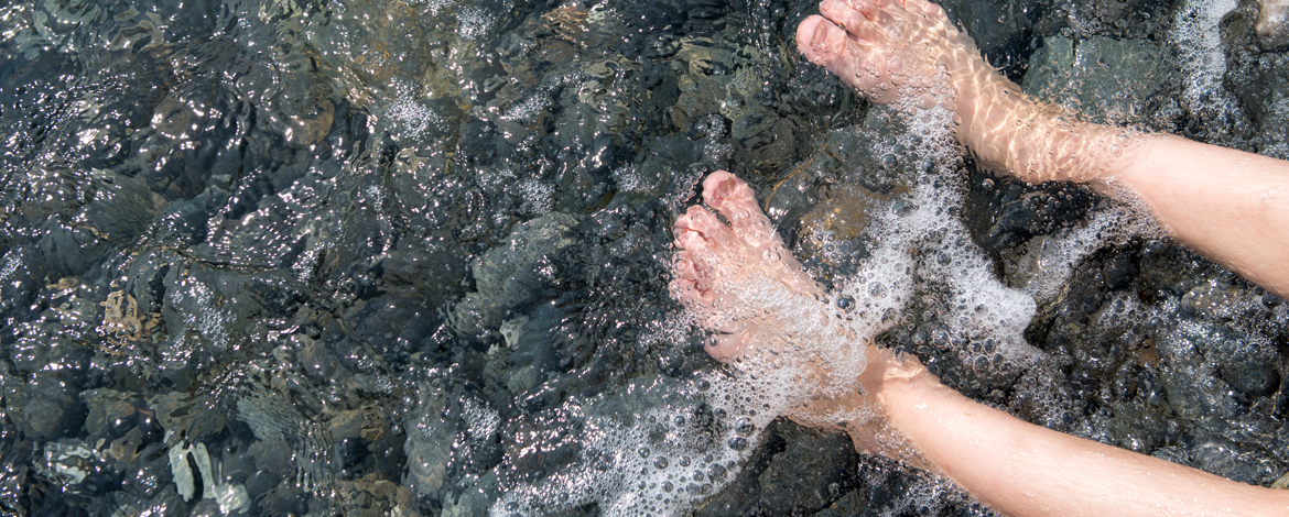 Someone with bare legs and feet sitting on rocks with their feet in the water.