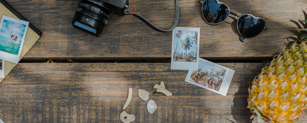 A table with a camera, Polaroid pictures, heart sunglasses, and a pineapple all sitting on it